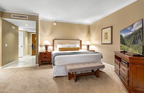A hotel room with a bed, bedside lamps, a bench, a dresser, and a television.