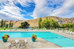 Una piscina con sillones de descanso, plantas en macetas y montañas al fondo.