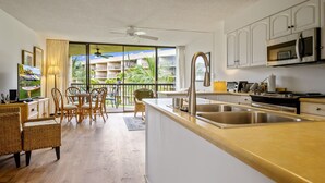 Et moderne køkken med en stor ø, rustfrie hvidevarer og udsigt til en balkon med udendørs møbler.