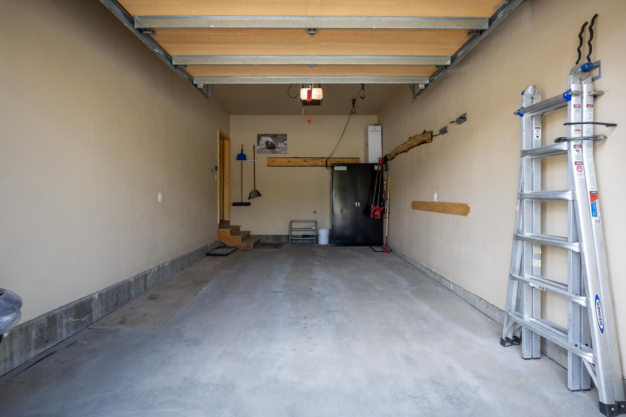 Un passadís estret amb sòl de formigó, una porta de fusta al final i una escala recantant contra la paret.