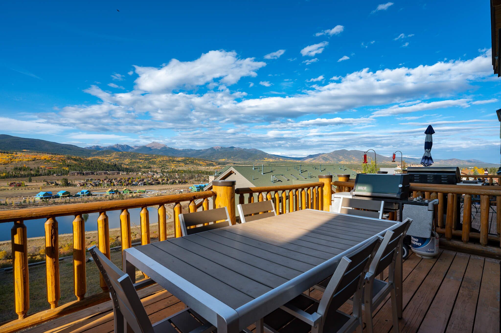 A deck with a table and chairs, overlooking a scenic view of mountains and a lake.