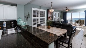 A modern kitchen with a granite countertop, white cabinets, and a dining area with a black leather couch.