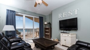A living room with a large TV, leather sofas, a coffee table, and a ceiling fan.