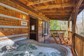 Una cabaña de madera con jacuzzi, terraza de madera y mobiliario exterior.