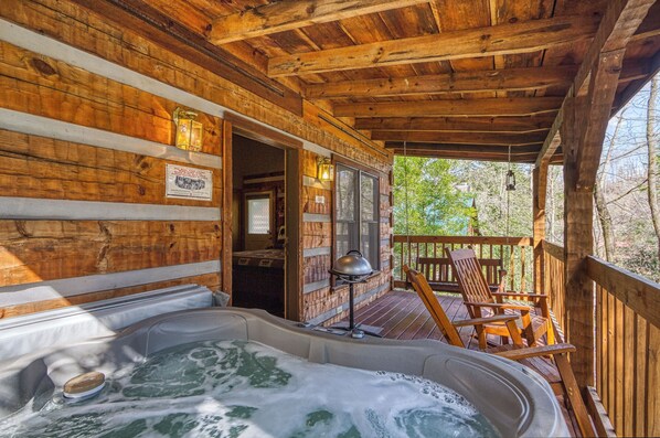 A wooden cabin with a hot tub, wooden deck, and outdoor seating.