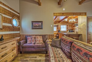 A cozy living room with a wooden wall, a leather sofa, a patterned couch, and a wooden cabinet.
