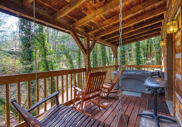 A wooden deck with rocking chairs and a grill, overlooking a forested area.