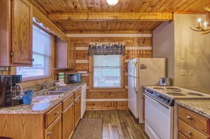 A compact kitchen with wooden cabinetry, a built-in stove, a refrigerator, and a microwave.