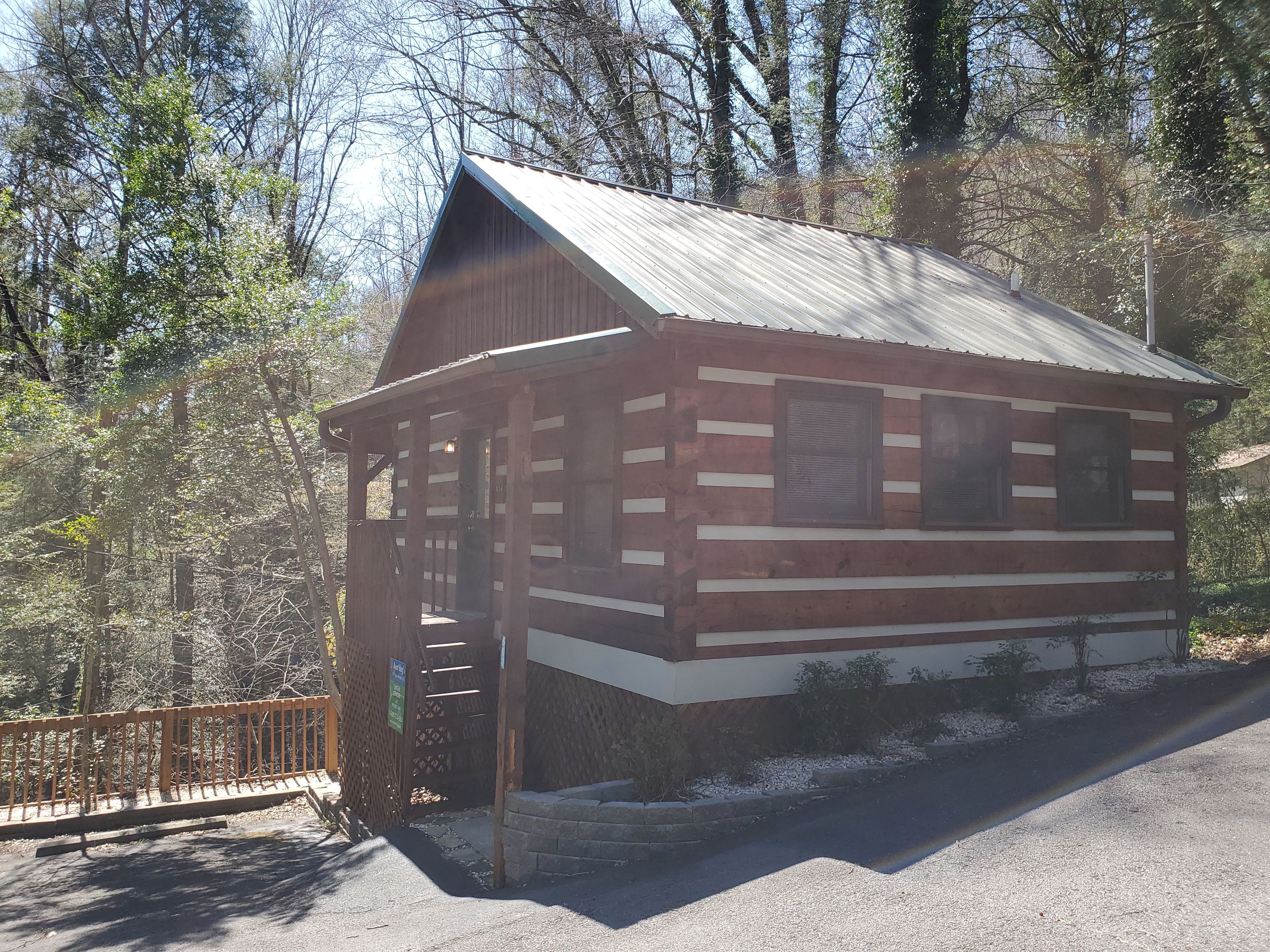 A small wooden cabin with a porch and a metal roof, surrounded by trees.