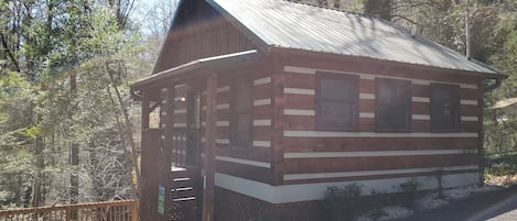 A small wooden cabin with a porch and a metal roof, surrounded by trees.