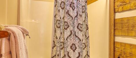 Zona de ducha con cortina de baño estampada, una bañera blanca y una pared de madera.