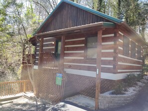 A wooden cabin with a porch, a fenced yard, and a number sign.