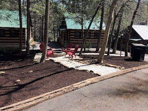 A rustic cabin with a fire pit and red chairs in a wooded area.