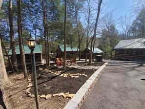 A forested area with log cabins, a paved path, and outdoor seating.