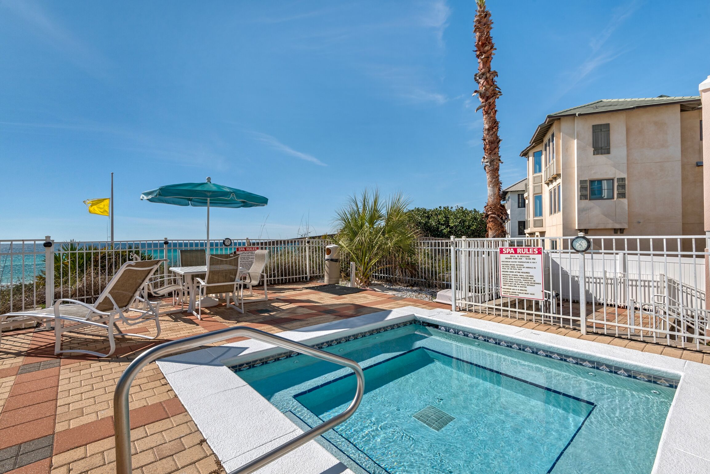 A pool area with a clear view of the ocean, a flag, and a sign indicating spa rules.