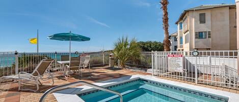A pool area with a clear view of the ocean, a flag, and a sign indicating spa rules.
