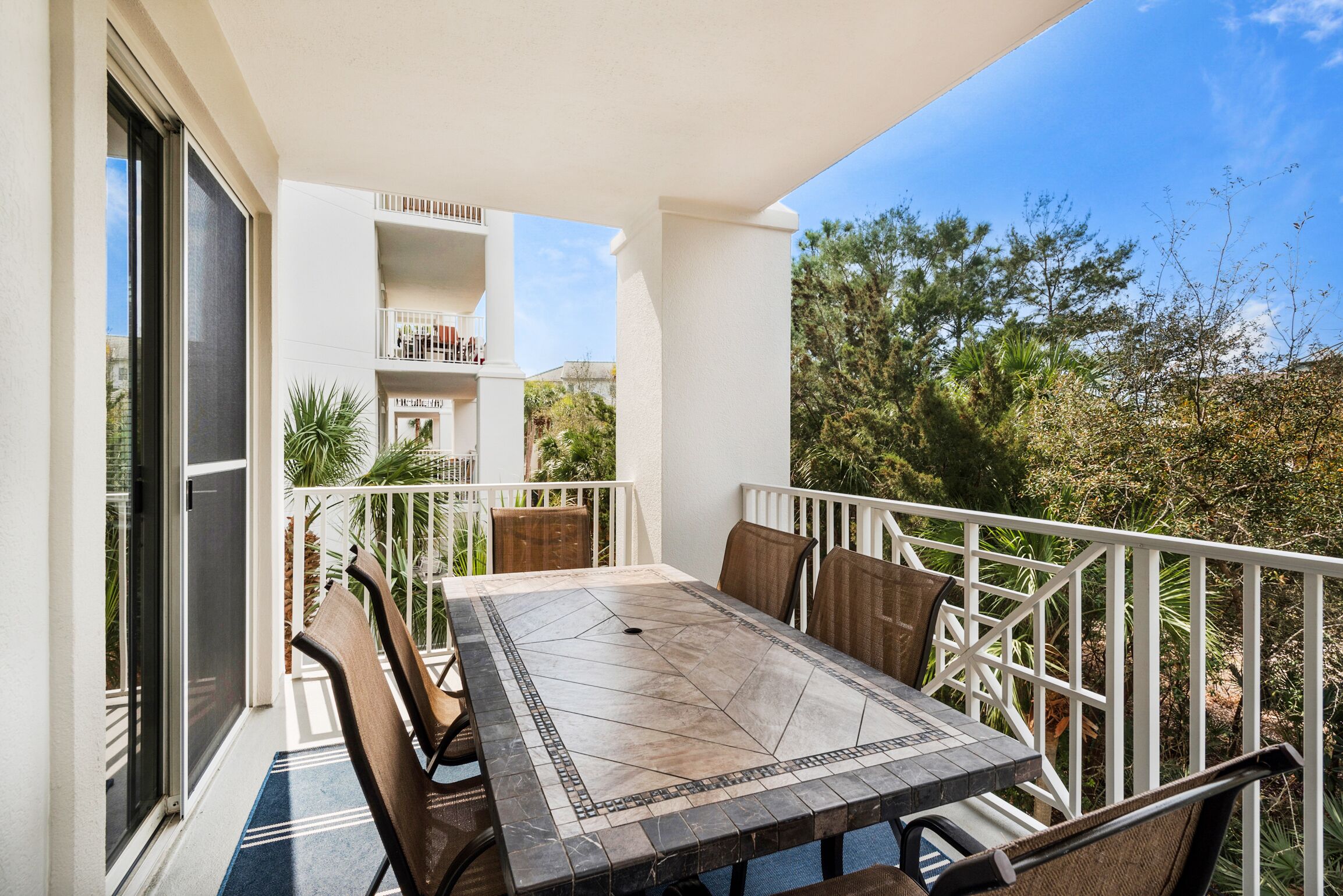 Un balcon avec une table et des chaises, une balustrade blanche et une vue sur la verdure et les bâtiments.