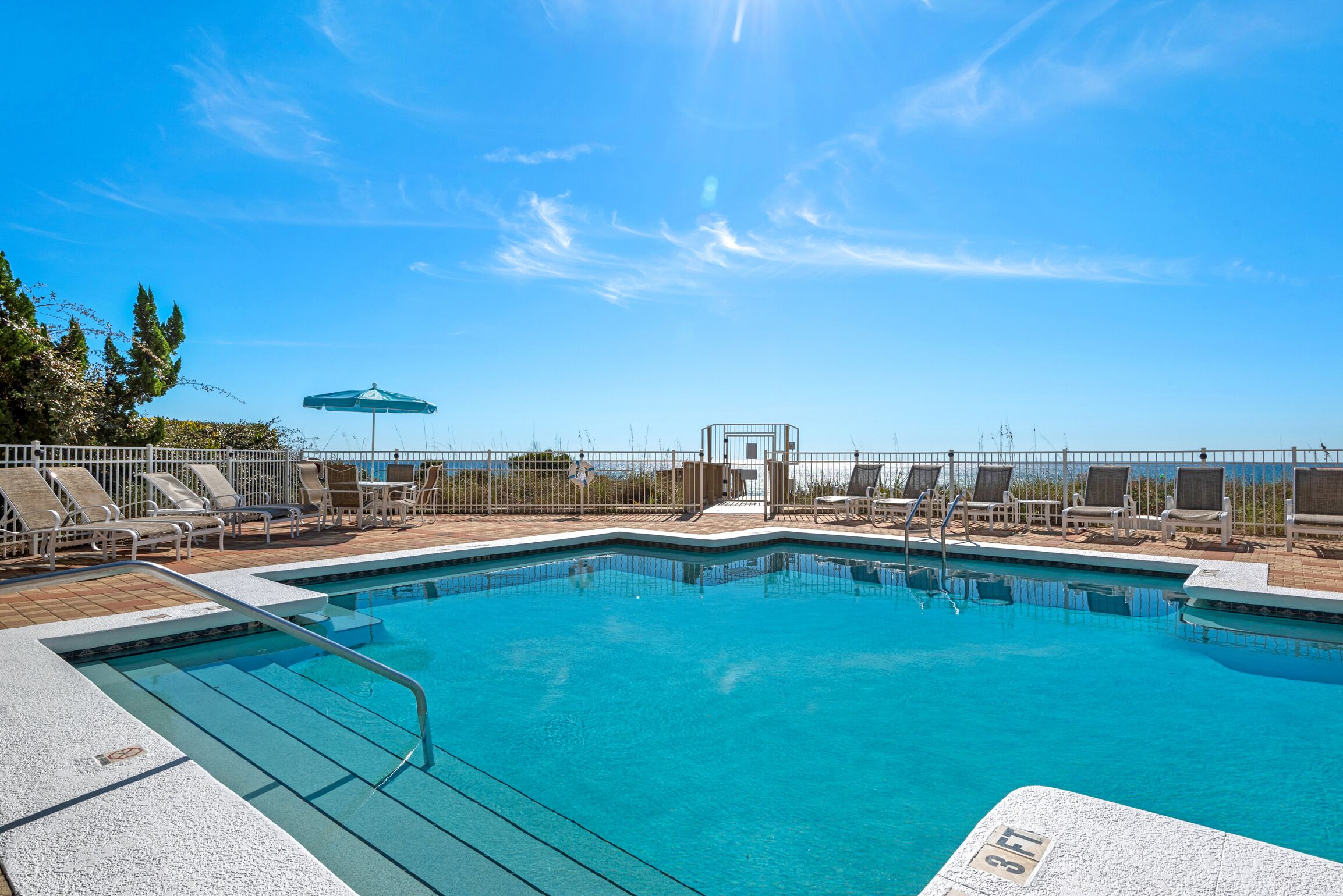 Une piscine rectangulaire dotée d’une rambarde métallique, entourée de chaises longues et d’une clôture.