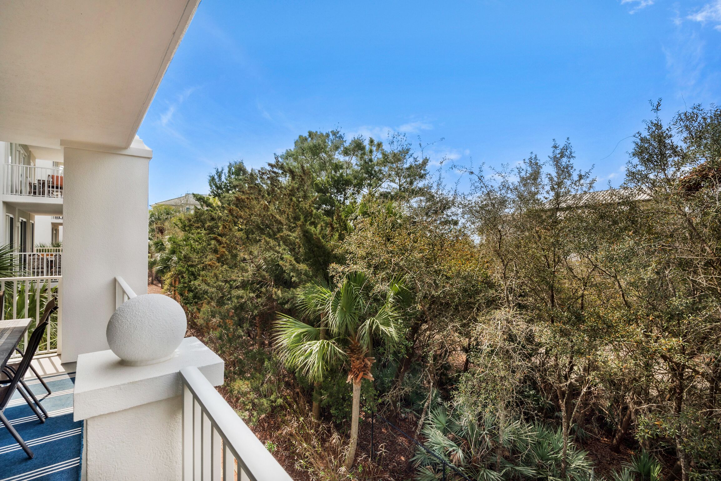 A balcony with a white railing, a round white object on the railing, and a view of dense greenery and trees.