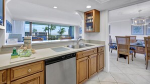 A modern kitchen with a dishwasher, wooden cabinets, a built-in sink, and a window overlooking palm trees.