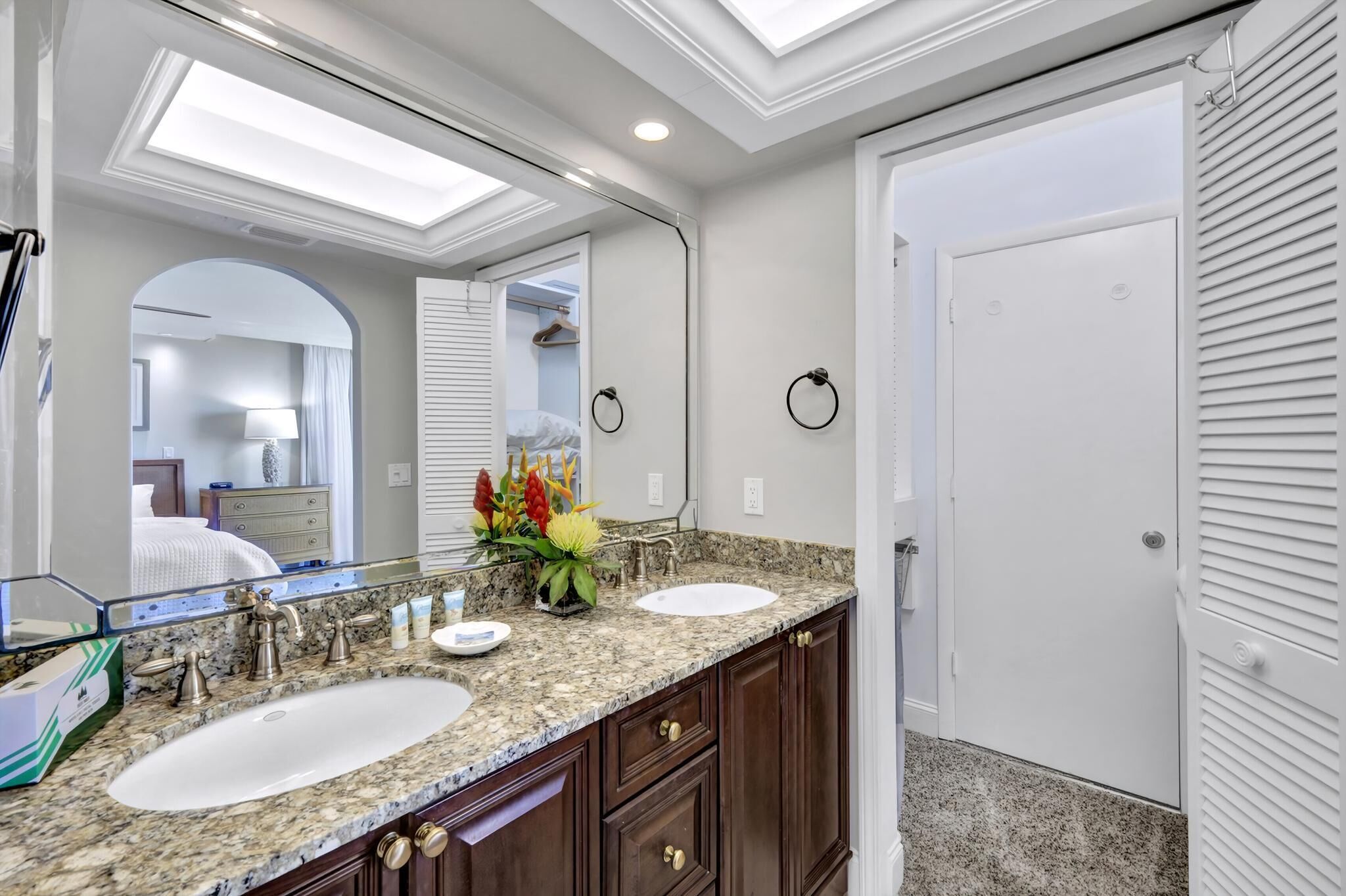 A bathroom with two sinks, a large mirror, and a door leading to another room.