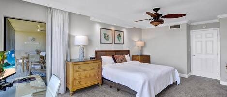 Una habitación de hotel con cama, escritorio, silla, cómoda y ventilador de techo.