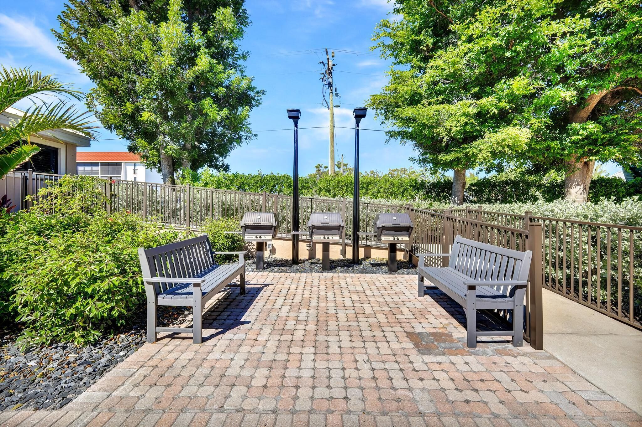 An outdoor patio with brick flooring, two benches, and a metal fence.