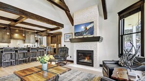 A spacious living room with a fireplace, a dining area with wooden chairs, and a kitchen with dark wood cabinets.