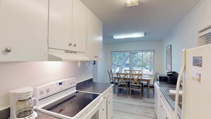 A compact kitchen with white cabinets, a coffee maker, a stove, and a dining area with a table and chairs.