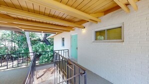 A covered outdoor area with a wooden ceiling, a white brick wall, a turquoise door, and a window with blinds.