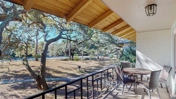 A covered outdoor patio with a table and chairs, surrounded by trees and a view of a park.