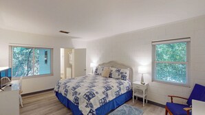 A bedroom with a bed, bedside tables, a chair, and windows with blinds.