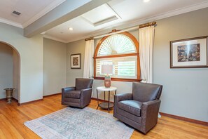 A room with two leather armchairs, a patterned rug, a small round table with a lamp, and a large arched window with curtains. - 20-Acre Estate w/ Pool, Games & Meeting Space (Oakland)