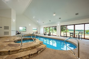 A large indoor swimming pool with stone steps and metal railings, surrounded by lounge chairs and a patio area with a view of greenery. - 20-Acre Estate w/ Pool, Games & Meeting Space (Oakland)