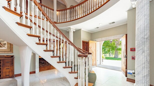 A grand staircase with white balustrades and wooden steps, leading to a room with a marble floor and a view of a green outdoor area. - 20-Acre Estate w/ Pool, Games & Meeting Space (Oakland)
