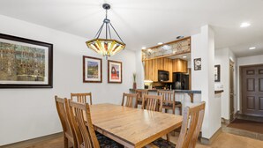 A dining area with a wooden table and chairs, a hanging light fixture, and kitchen cabinets in the background. - Ski-in/Ski-Out Ground Floor Easy Access Ski Condo (Telluride)
