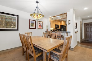 Un coin repas avec une table et des chaises en bois, un luminaire suspendu et des meubles de cuisine en arrière-plan.