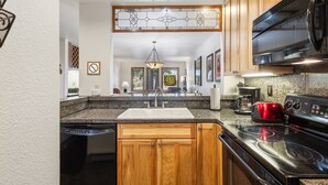A kitchen with wooden cabinets, a granite countertop, a stainless steel stove, and a red toaster. - Ski-in/Ski-Out Ground Floor Easy Access Ski Condo (Telluride)