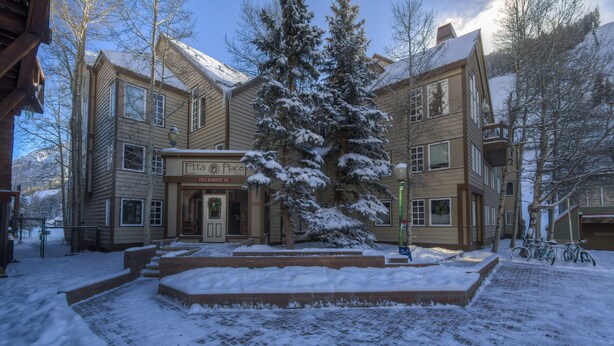 A two-story building with a snow-covered entrance and a large evergreen tree in front. - Ski-in/Ski-Out Ground Floor Easy Access Ski Condo (Telluride)