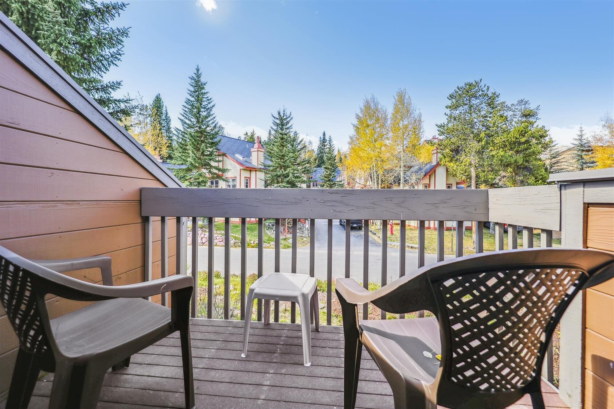 A wooden deck with two chairs and a small table, overlooking a residential area with houses and trees.