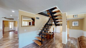 A spacious living area with a wooden staircase, a large mirror, and a dining area.