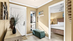 Una habitación con cama, un banco, una puerta y una pared con un cartel.