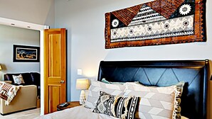 Une chambre d’hôtel avec un grand lit, une porte en bois, une œuvre d’art accrochée au mur et une petite table avec une lampe.