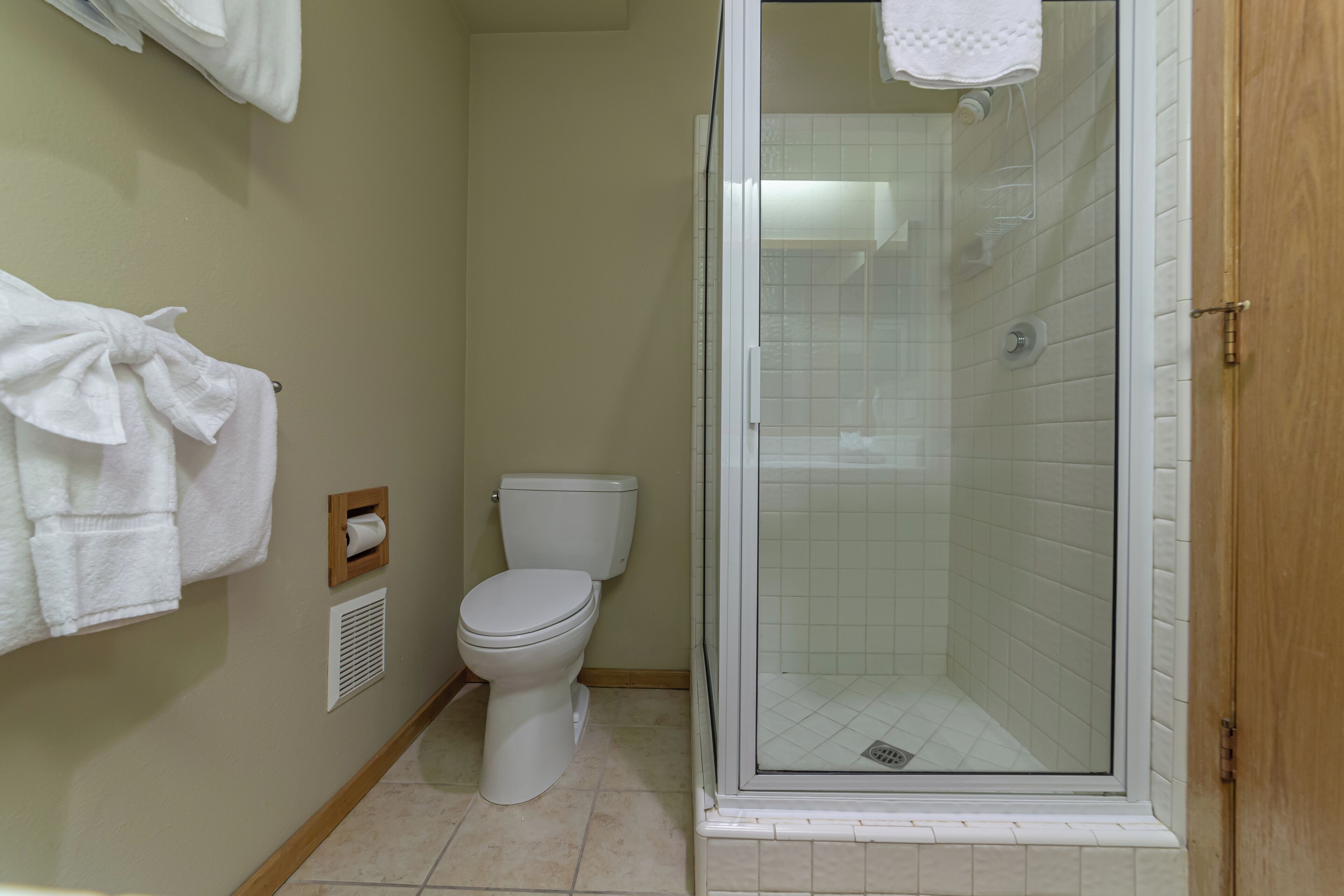 A bathroom with a toilet, a shower with a glass door, and a towel rack with towels.