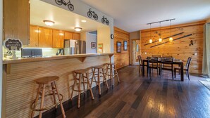 A kitchen with wooden cabinets, a refrigerator, and a bar area with stools. - Scenic Family-Friendly Condo w/ Spa 307 (Mammoth Lakes)