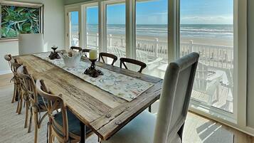 Un espace repas comprenant une grande table, des chaises et une vue sur la plage grâce à de larges fenêtres.