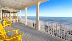 Un'area esterna coperta con poltrone Adirondack gialle, un parapetto bianco e vista sulla spiaggia e sull'oceano.