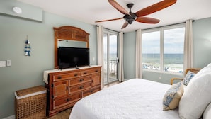 A bedroom with a large bed, wooden dresser, television, and a view of the ocean through large windows. - Island Princess 509🌊Gulf Front🏖️Free Beach Setup (Fort Walton Beach)