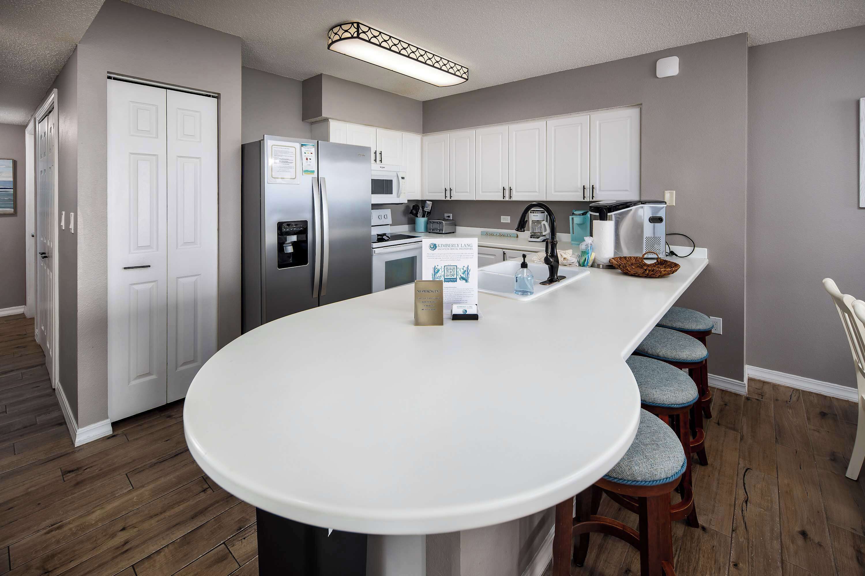 Une cuisine moderne avec des meubles blancs, un îlot central doté de tabourets de bar, des appareils en acier inoxydable et un luminaire suspendu.