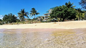Een strandhotel met helder ondiep water, palmbomen en een zandstrand.
